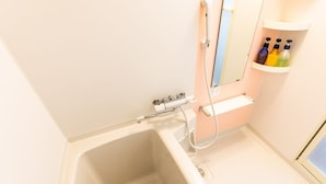 A bathroom with a bathtub, a shower, and a shelf with toiletries. - Hotel T-style (Naha)