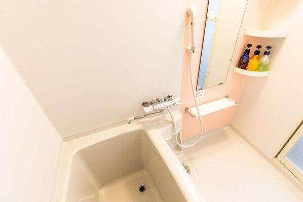 A bathroom with a bathtub, a shower, and a shelf with toiletries. - T Style (Naha)