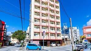 A multi-story building with a red and beige facade, air conditioning units on each floor, and a parking sign indicating a 500 yen fee. - Hotel T-style (Naha)