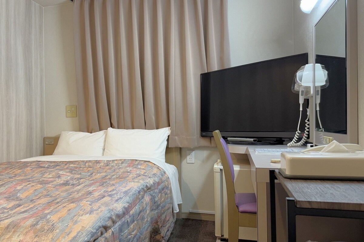 A hotel room with a bed, a desk with a computer, a television, and a telephone.