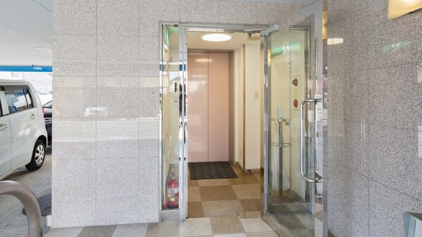 A hotel entrance with a glass door, a fire extinguisher, and a tiled floor. - Business Hotel East Park Ritsurin (Takamatsu)