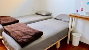 Une chambre avec deux lits simples, un bureau en bois, une poubelle blanche et une fenêtre.