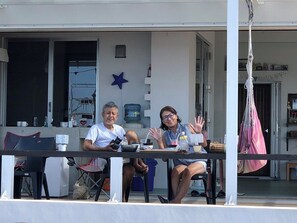 Two people seated at a table on an outdoor patio with a water dispenser, chairs, and a star decoration on the wall. - Umiyado Gohan Pork Luncheon Meat (Miyakojima)