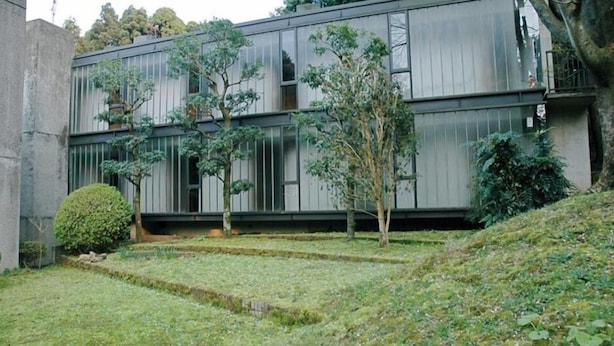 Ein modernes Gebäude mit flachem Dach, großen Fenstern und einem Innenhof mit Gras und Bäumen.
