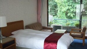 Ein Hotelzimmer mit Bett, Sessel, Tisch und Fenster mit Blick auf Bäume.