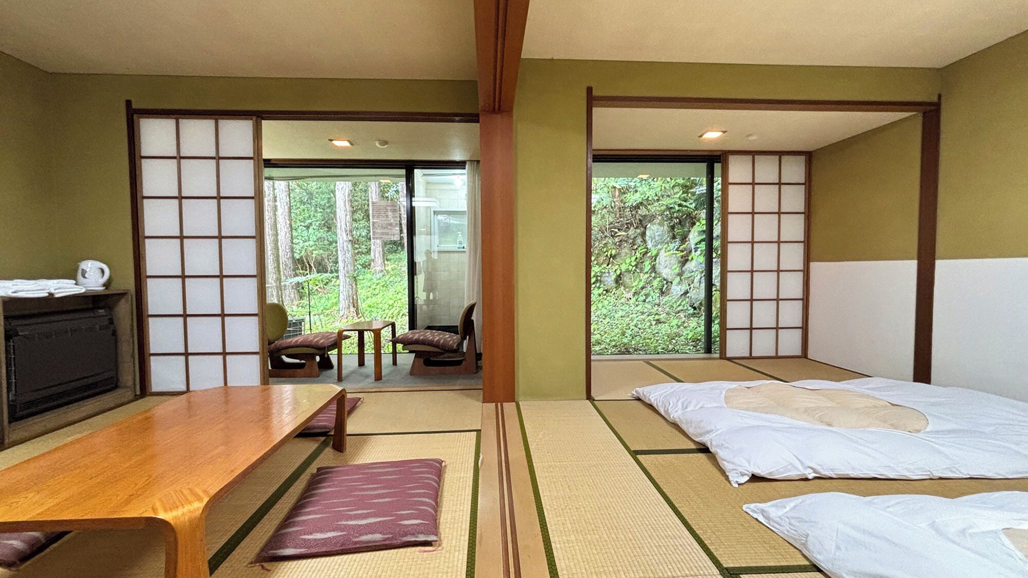 A traditional Japanese-style room with tatami flooring, a low wooden table, a sofa, and a bed with white bedding.