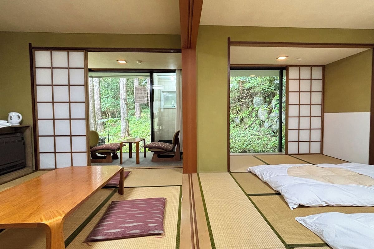A traditional Japanese-style room with tatami flooring, a low wooden table, a sofa, and a bed with white bedding.