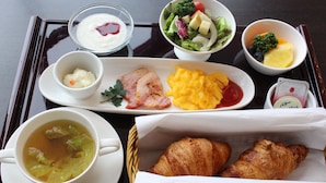 Ett bricka med frukosttillbehör, inklusive soppa, croissanter, äggröra, bacon och en sallad.