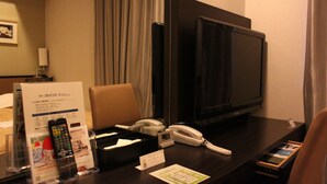 Ett hotellrum med en TV, en telefon, en fjärrkontroll, ett tidningsställ och en informationsskylt med information om rummet.