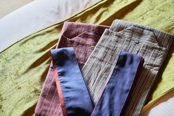A bed with a green blanket and multiple folded shirts in various colors and patterns. - Musubi no Koyado En (Kobe)