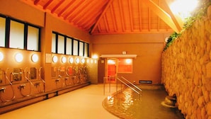A traditional Japanese onsen with multiple bathing areas, a stone wall, and a wooden ceiling. - Musubi no Koyado En (Kobe)