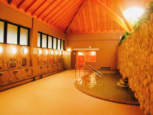 A traditional Japanese onsen with multiple bathing areas, a stone wall, and a wooden ceiling. - Musubi no Koyado En (Kobe)