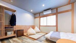 A traditional Japanese-style room with tatami flooring, a low wooden bed, a futon, a wardrobe with hanging clothes, and a window with shoji screens. - Musubi no Koyado En (Kobe)
