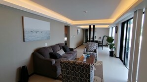 Uma sala de estar moderna com um sofá, poltronas estampadas, uma mesa de centro e uma área de jantar com mesa e cadeiras.