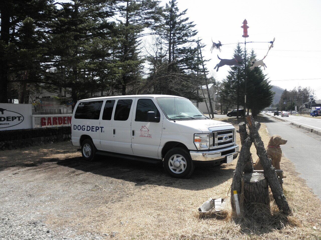 A white van parked on a gravel area with a dog statue and a sign for DOGDEPT.
