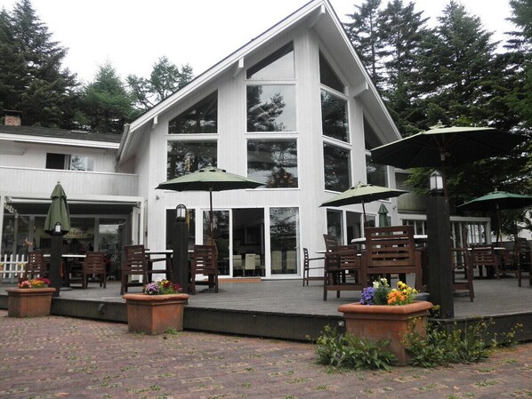 Un bâtiment à l’extérieur blanc, doté de grandes fenêtres et d’un espace extérieur aménagé avec des tables et des parasols.