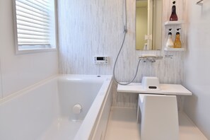 Une salle de bain moderne équipée d’une baignoire, d’un pommeau de douche à main, d’un thermostat numérique et d’une étagère pour les articles de toilette.