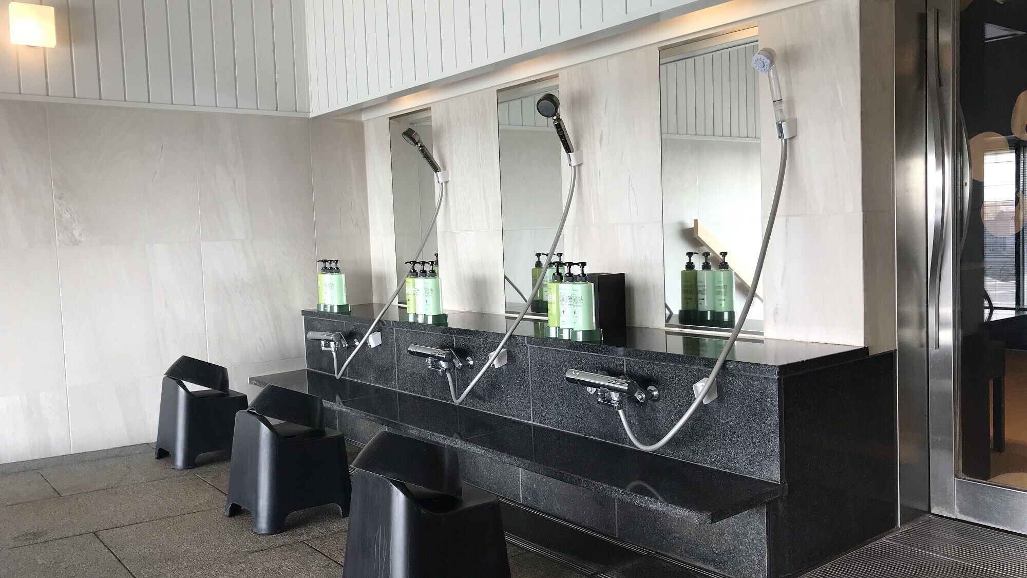 A modern bathroom with a black granite vanity, three sinks, and a large mirror.