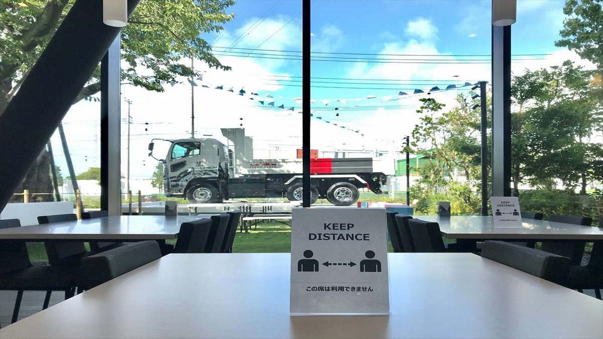 A restaurant with a 'KEEP DISTANCE' sign, outdoor seating, and a view of a truck on the street.