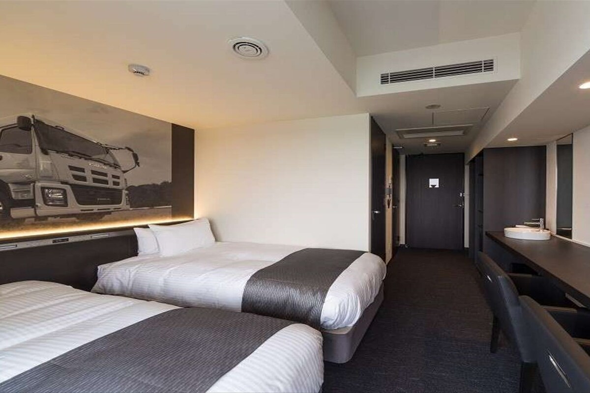 A hotel room with two beds, a desk, and a large painting on the wall.