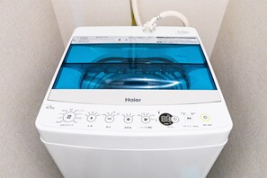 A white Haier washing machine with a transparent water tank, control panel with multiple settings, and a power cord plugged in. - Mr. Kinjo in Motobu (Motobu)