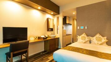 A hotel room with a bed, a desk with a chair, a TV, a sink, and a mirror.