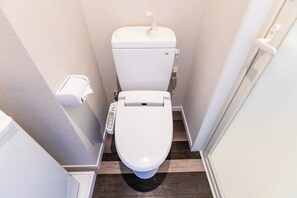 A small, modern bathroom with a white toilet, a control panel, and a toilet paper holder. - Mr. Kinjo in Motobu (Motobu)