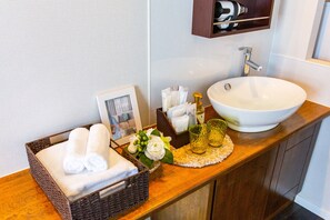 A bathroom with a white sink, a framed photo, a basket of towels, and toiletries on the counter. - Mr. Kinjo in Motobu (Motobu)