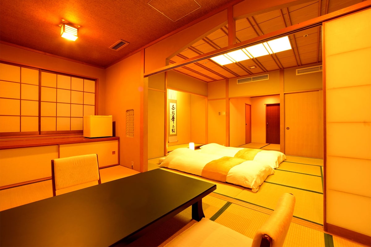 Una habitación japonesa tradicional con suelo de tatami, una mesa baja y una cama con ropa de cama estilo futón.