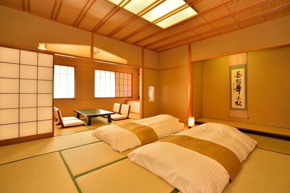 Una habitación japonesa tradicional con suelo de tatami, una mesa baja y una cama con ropa blanca.