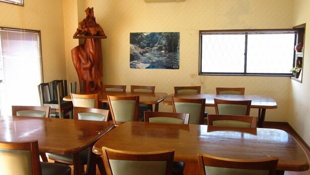 A dining area with wooden tables and chairs, a large wooden sculpture, and two paintings on the walls. - Minshuku Miyoshiya <yakushima> (Yakushima)