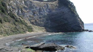Un paisaje costero con una formación rocosa destacada, una playa y aguas cristalinas.