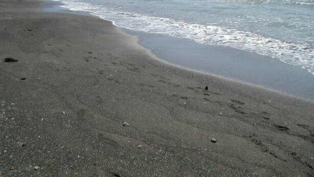 Una playa con arena, mar tranquilo y una tierra firme a lo lejos.