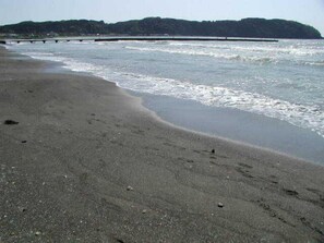 Una playa con arena, mar tranquilo y una tierra firme a lo lejos.
