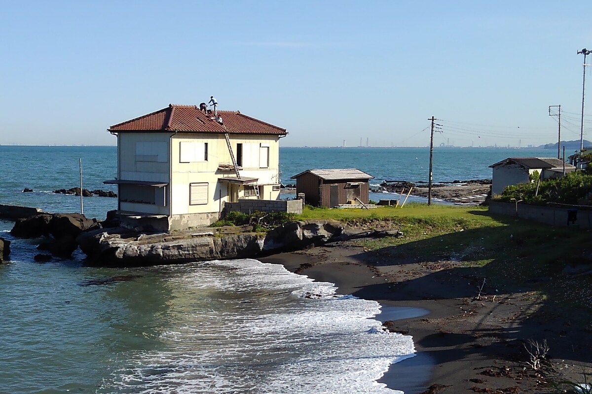 A coastal building with a red-tiled roof, situated on a rocky shoreline with a view of the sea.