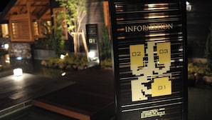 Ein digitales Informationshäuschen mit Pixel-Design, gelegen in einem gut beleuchteten Außenbereich mit Holzelementen und Pflanzen im Hintergrund.