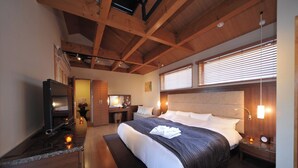 Ein modernes Hotelzimmer mit einem großen Bett, Holzbalkendecke, einem Fernseher und einer kleinen Schreibtischzeile.