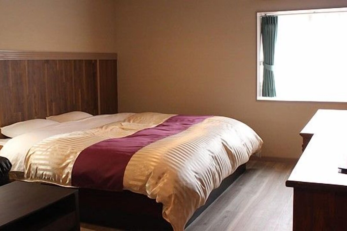A hotel room with a bed, a nightstand, a desk, and a window with curtains.