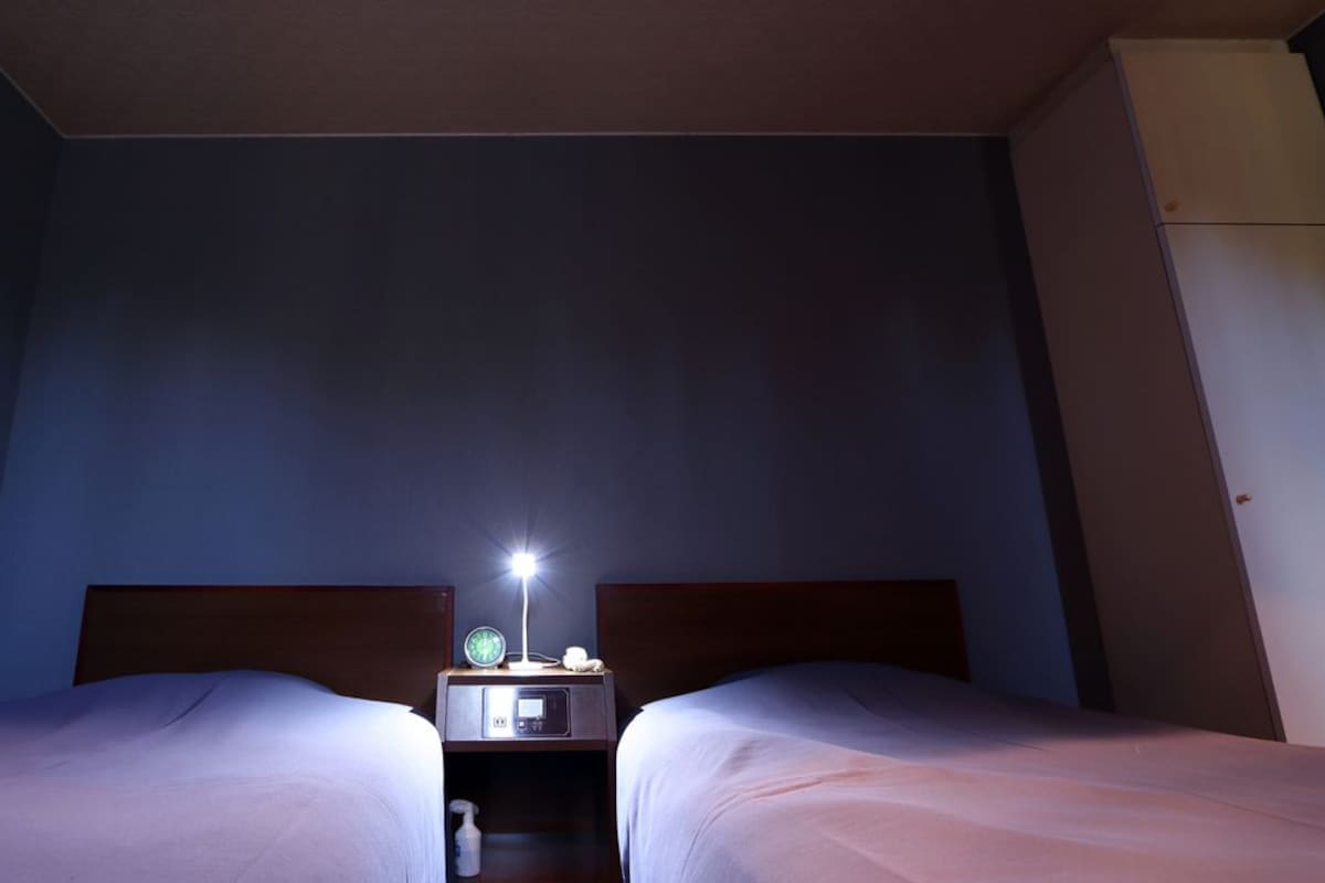 A hotel room with two beds, a nightstand with a lamp, and a small table.