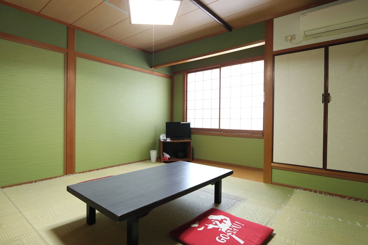 A room with tatami flooring, a low table, a television on a stand, and a wardrobe.