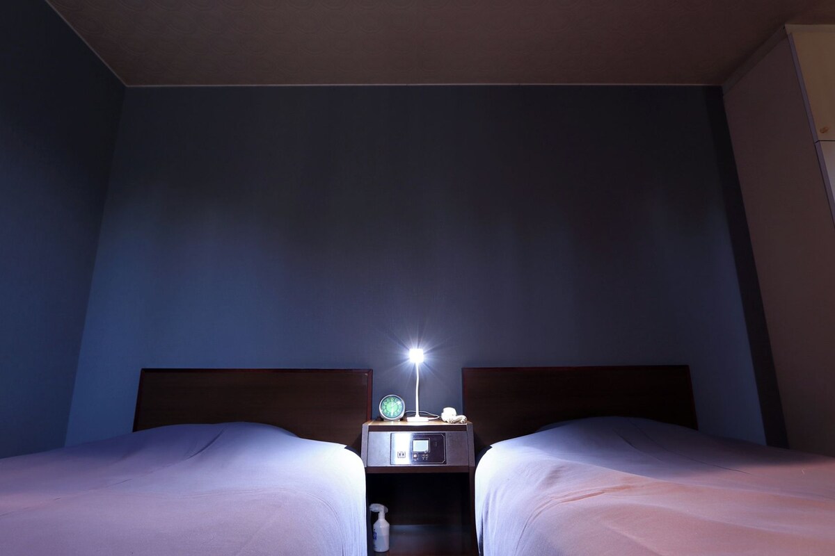 A hotel room with two beds, a nightstand with a lamp, and a wardrobe.