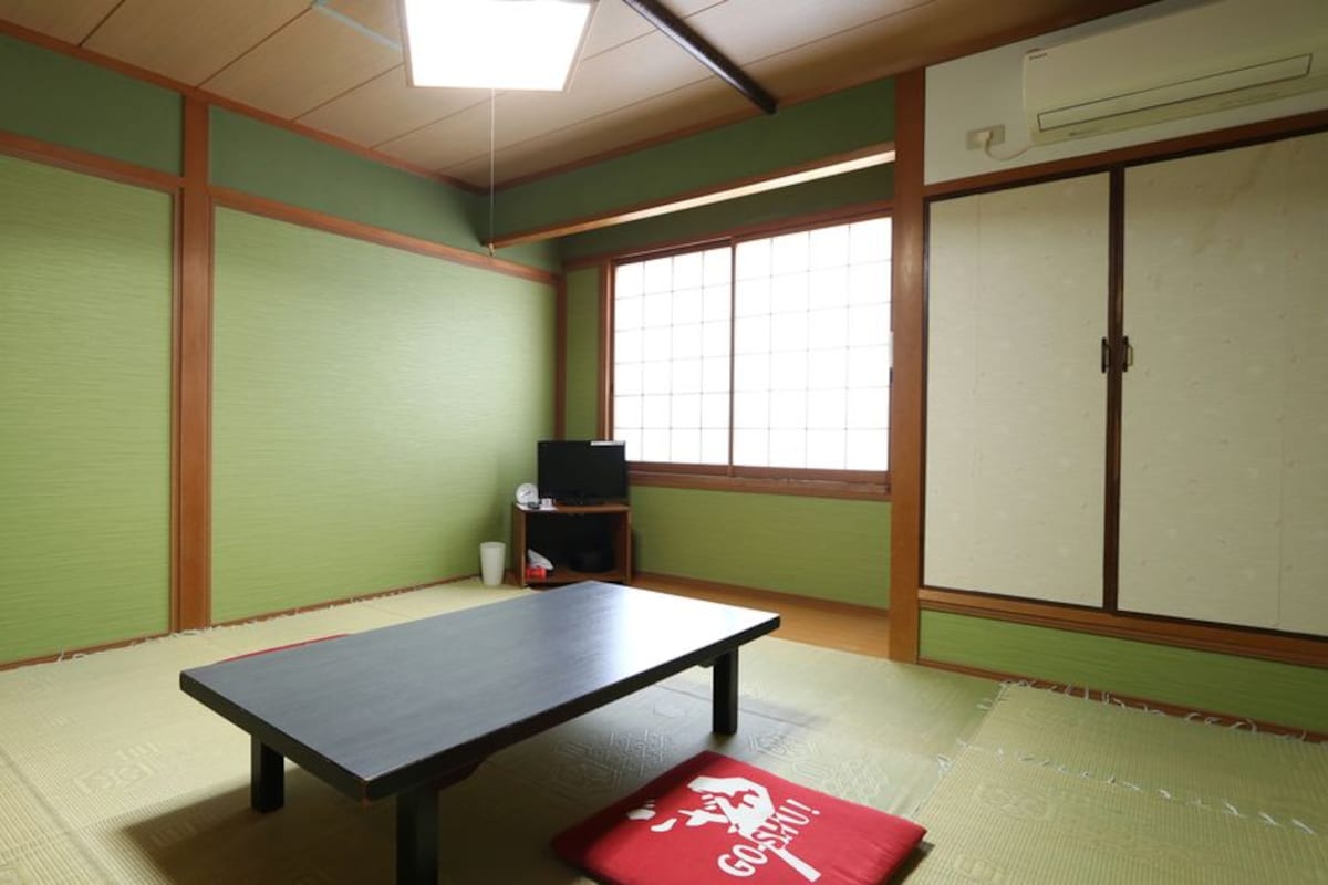 A traditional Japanese room with tatami flooring, a low table, a television, and sliding doors.