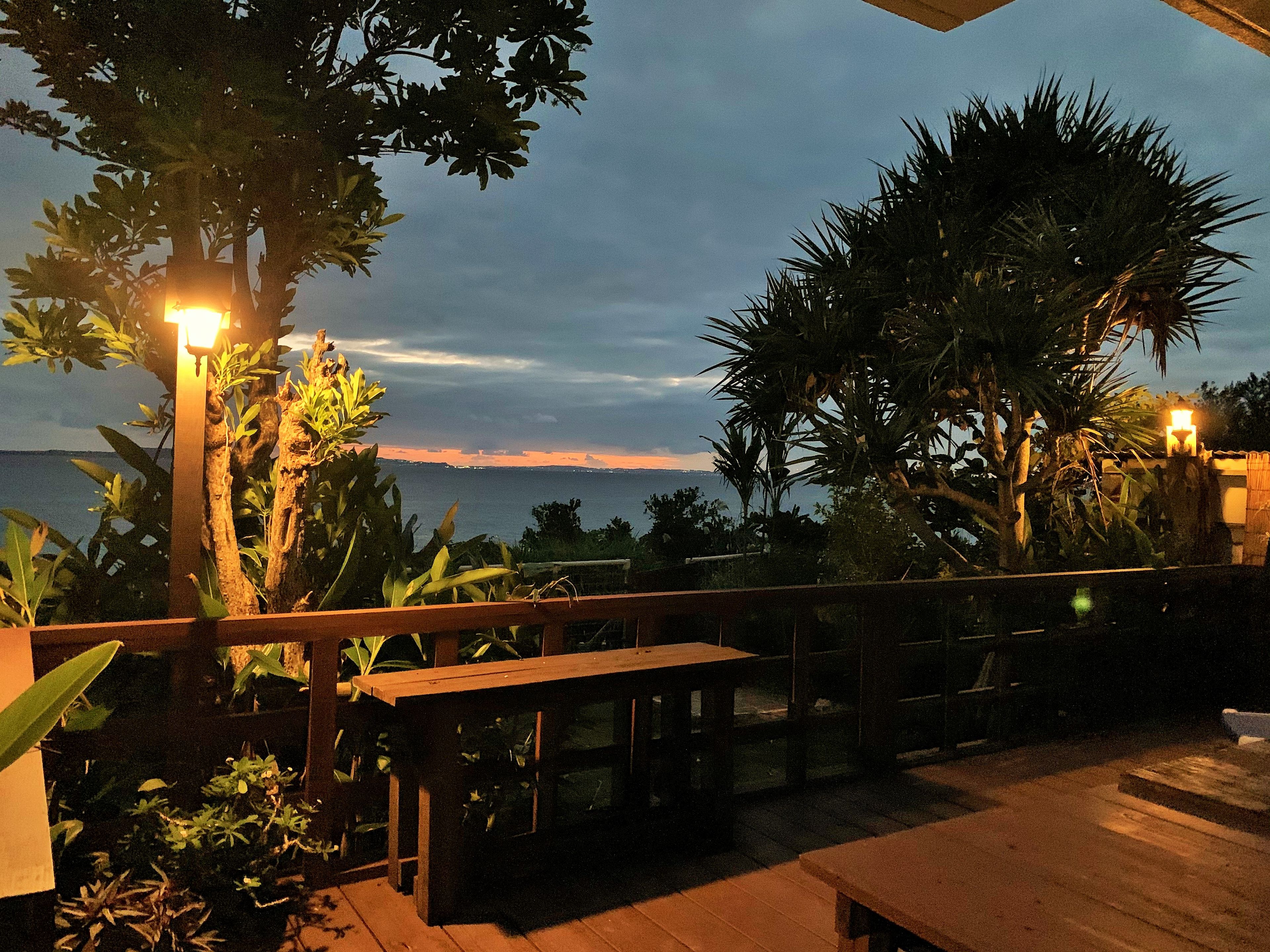 Un espace extérieur aménagé en terrasse, avec vue sur la mer, doté de meubles en bois et de plantes en pot.