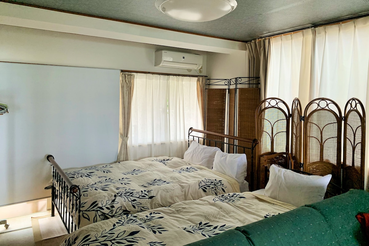 A bedroom with a single bed, a window with curtains, an air conditioning unit, and a green sofa.