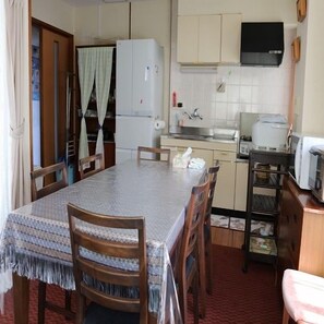A compact kitchen with a refrigerator, stove, and microwave. There is a dining table with chairs.