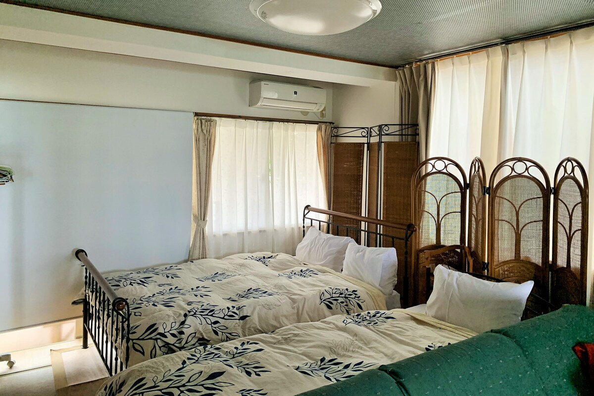 Een slaapkamer met een eenpersoonsbed, een raam met gordijnen, een airconditioning en een groene bank.