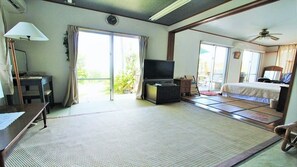 A hotel room with tatami flooring, a television, a bed, a desk, and a sliding door to a balcony. - Uminosoba Pension (Ginoza)
