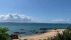 A beach with clear blue water, sandy shore, and scattered rocks.