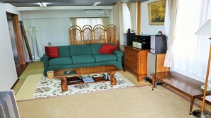 A living room with a sofa, a wooden coffee table, a cabinet, and a television. - Uminosoba Pension (Ginoza)