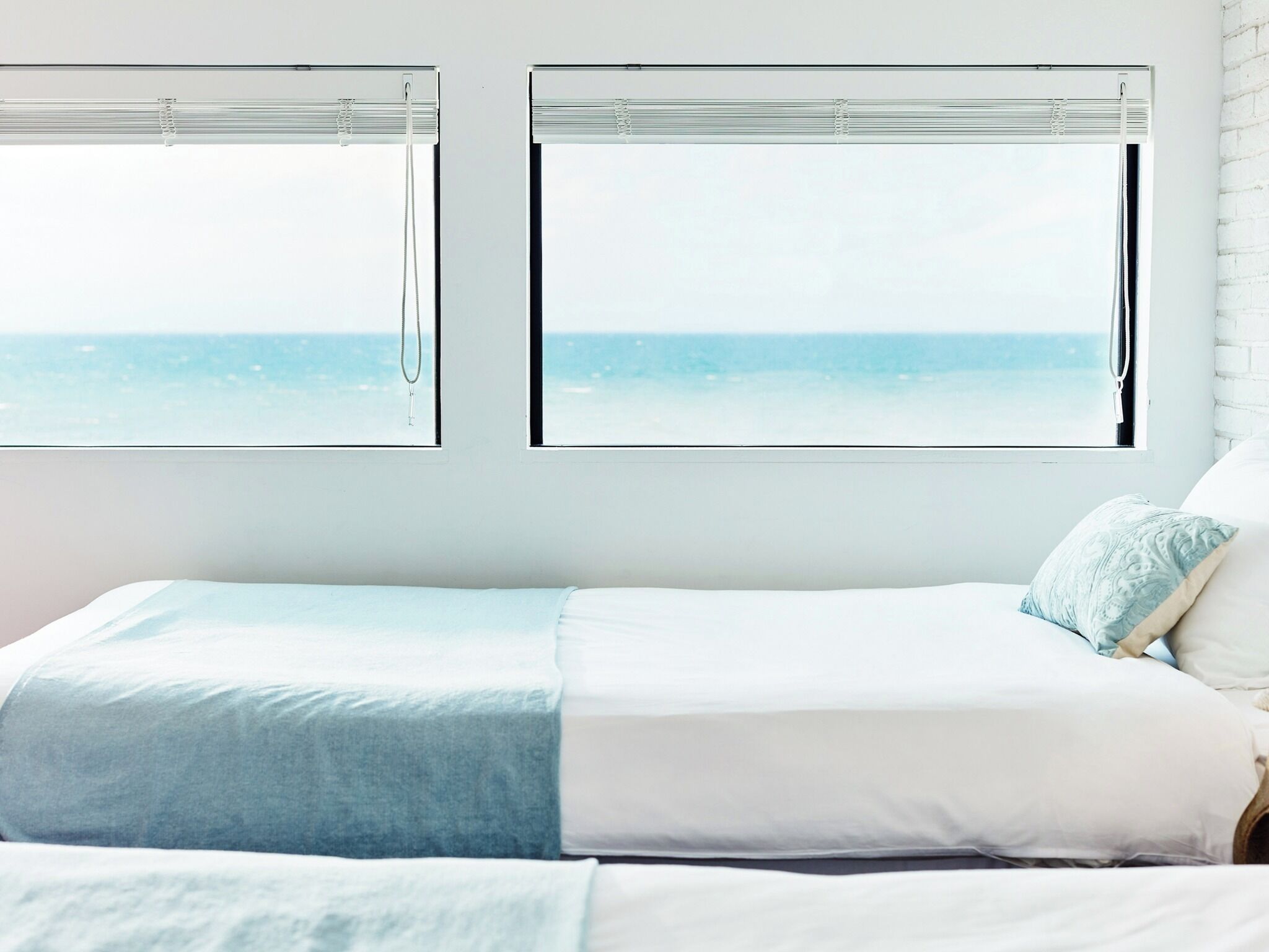 Une chambre à coucher avec un lit, deux fenêtres équipées de stores et une vue sur la mer.